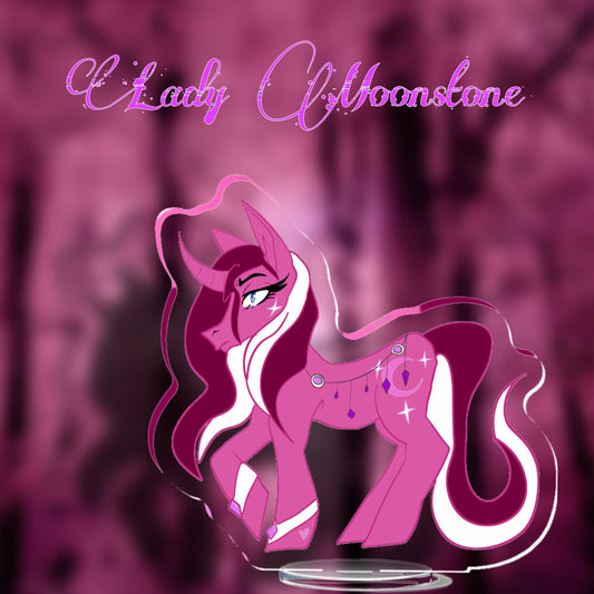 Lady Moonstone Standee Mockup
A Matte Rose unicorn with a wavy two toned, Siren Reddish Pink & White, mane and tail, her tail curls outwards at the end. She has Shocking White metal cuffs on her front hooves with Calypso Orchid Pink gems on the front. The same gems are strewn across her back, encased in the same Shocking White metal and chain with Electric Violet crystals hanging down. She has a white 4 pointed star on her cheek. The same 4 pointed stars shimmer around her Pink crescent moon cutie mark.